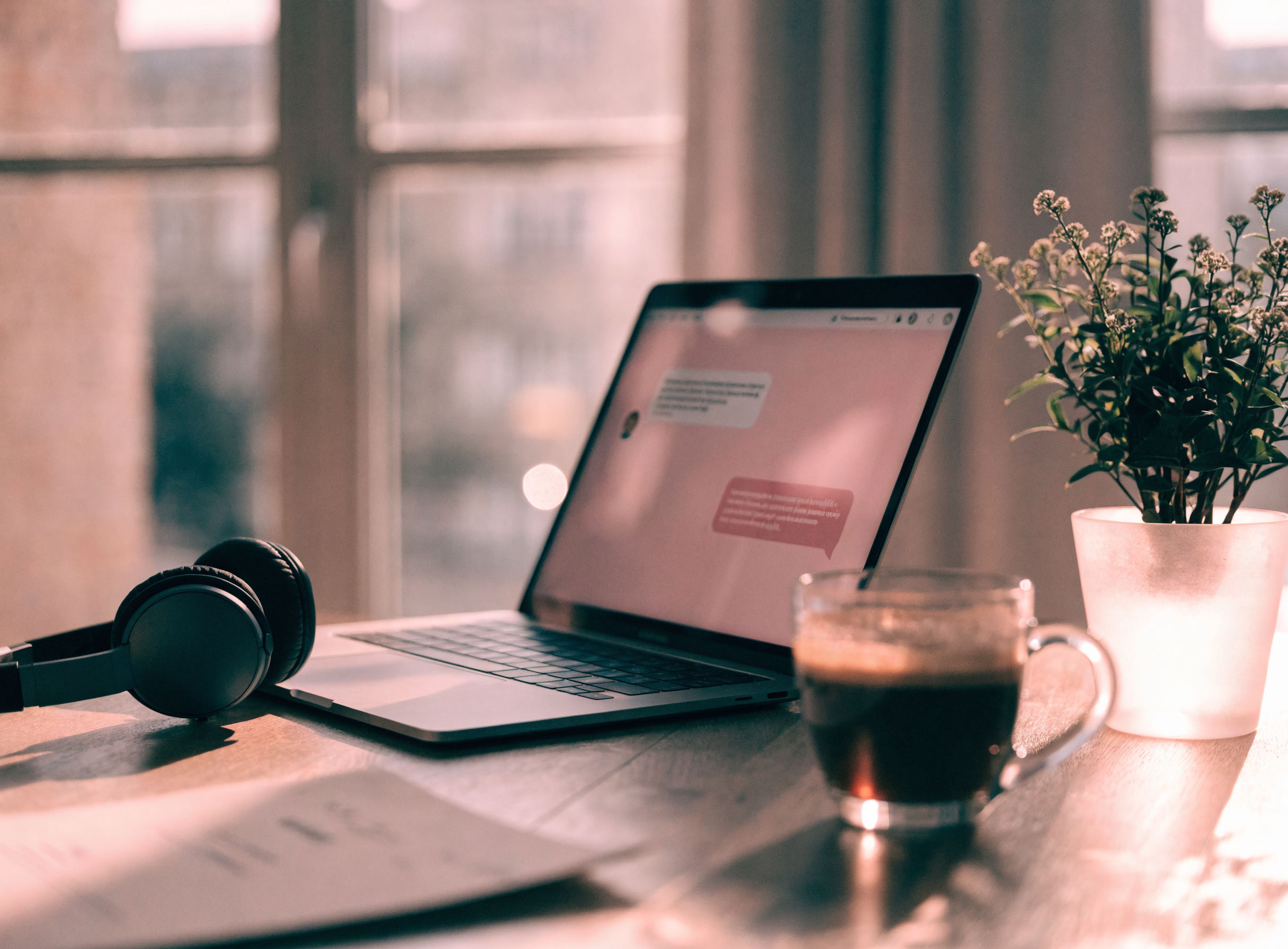 Gemütlicher Schreibtisch mit Laptop und Chat-Interface, Kopfhörern, Kaffeetasse und Pflanze — deutschsprachiges Chat-Team von Candy Creator Agency im DACH-Raum.