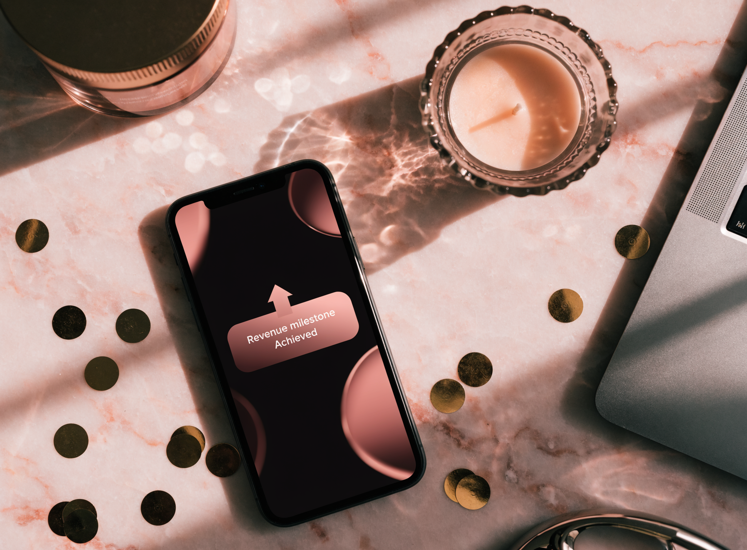 Smartphone auf Marmor-Tisch zeigt eine Revenue-Milestone-Erfolgsbenachrichtigung mit Konfetti — Umsatz-Meilenstein einer Creatorin, betreut von Candy Creator Agency.