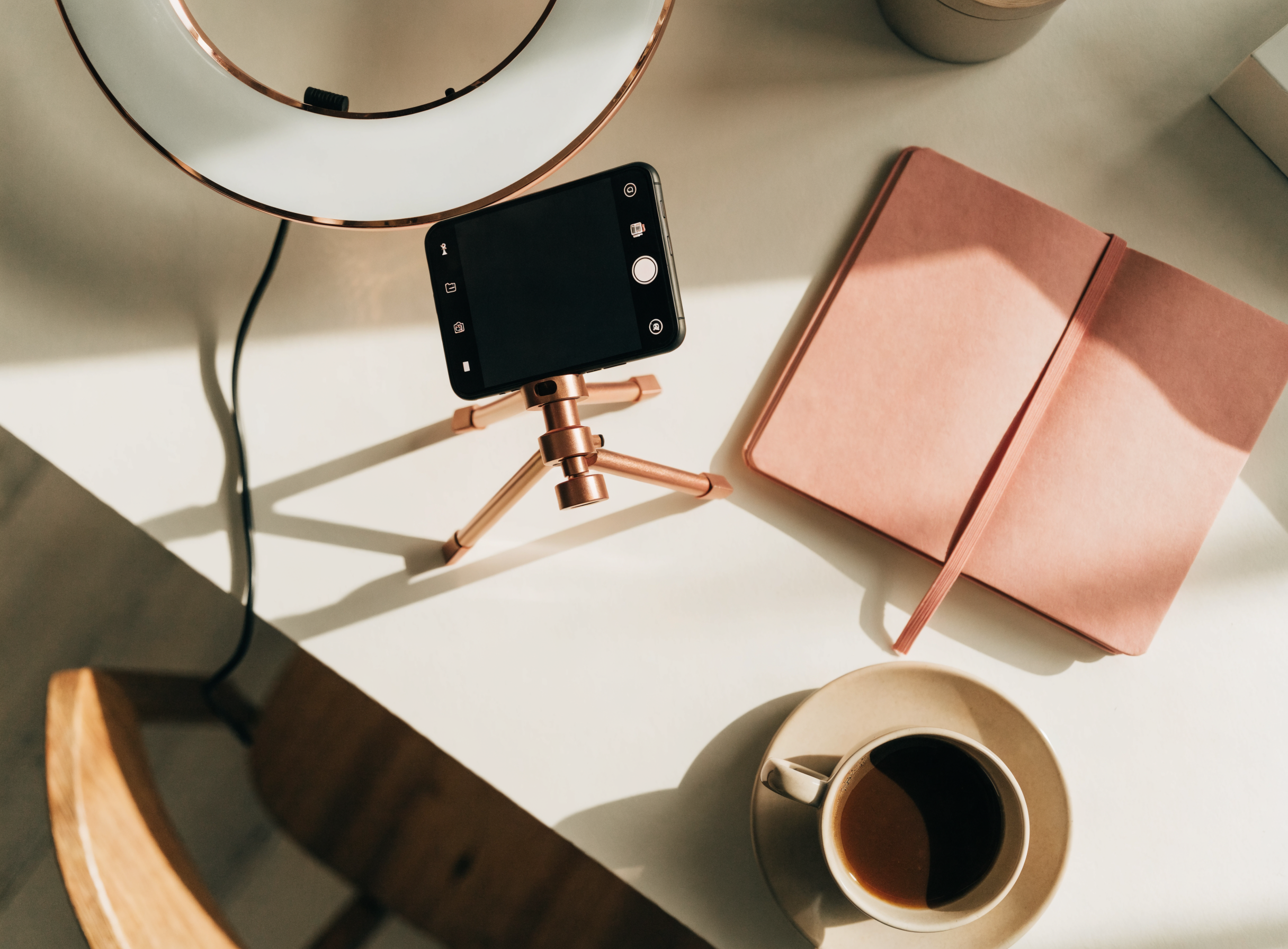 Content-Creator-Arbeitsplatz von oben: Ringlicht, Smartphone auf Stativ, rosé Notizbuch und Kaffeetasse — Symbol für professionelles OnlyFans-Management bei Candy Creator Agency.
